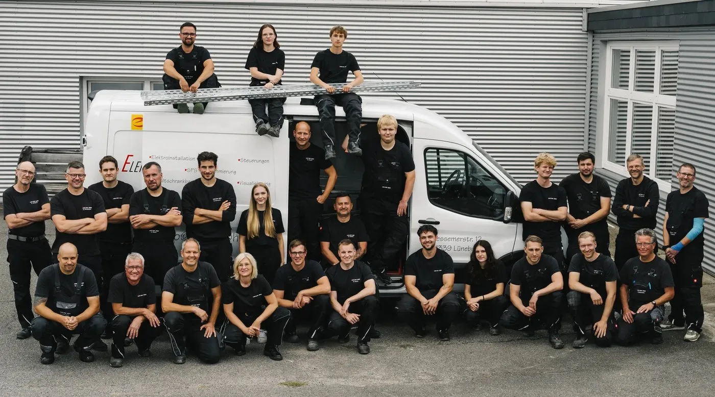 Das Team in schwarzer Arbeitskleidung vor und auf einem beschrifteten Firmentransporter