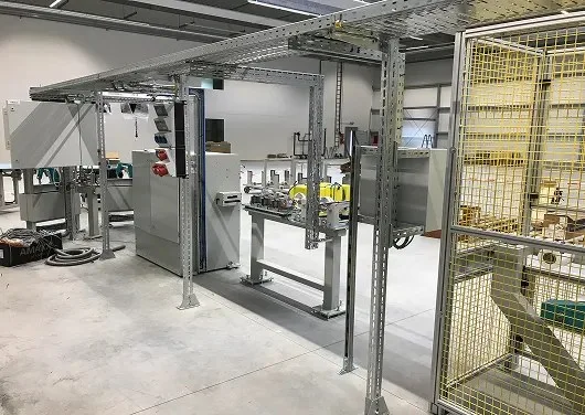 Stahlgerüst mit Kabeltrasse über einer Anlage in einer Werkhalle, daneben ein gelbes Schutzgitter