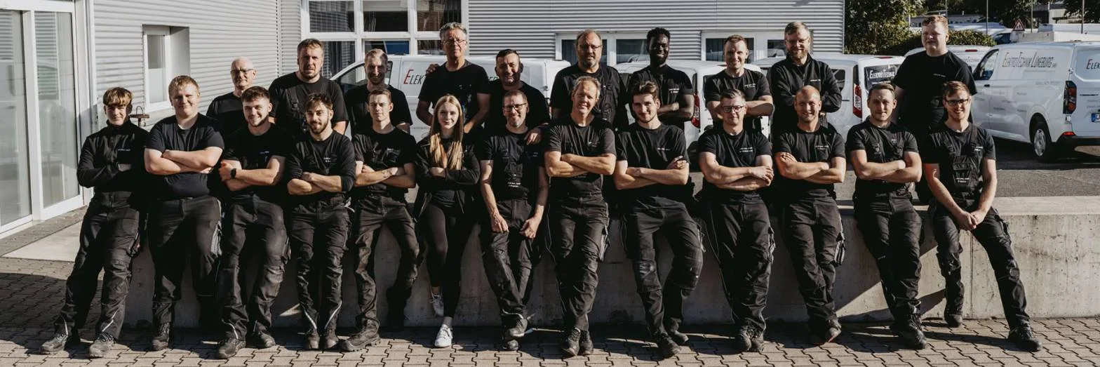 Das ETL-Team sitzt und steht in schwarzer Arbeitskleidung vor der Halle, dahinter Firmenwagen